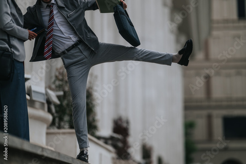 Bild auf Leinwand A businessman in a suit balances on a ledge while holding a briefcase