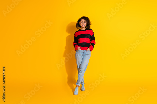 Fotografie Young woman in striped sweater poses against bright yellow backdrop for casual f
