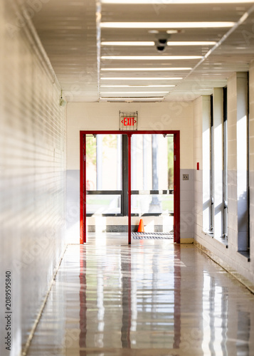 фотографія Empty school hallway with a glossy reflective floor leading toward red framed glass doors and a backlit exit sign