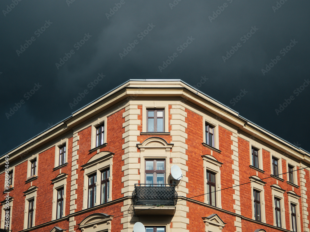 Fototapeta premium Narożnik zabytkowej kamienicy z cegły na tle ciemnego, burzowego nieba
