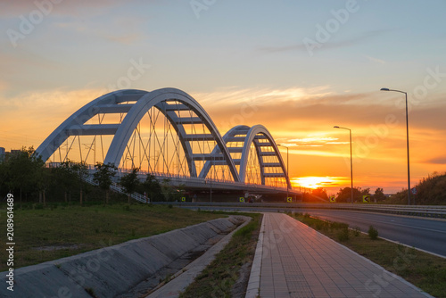 Tableau sur toile Bridge with arches over a roadway at sunset, urban landscape, lamps along the ri