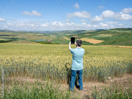 Man Using Tablet to Photograph Wheat Field and Scenic Countryside