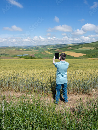 Man Using Tablet to Photograph Wheat Field and Scenic Countryside
