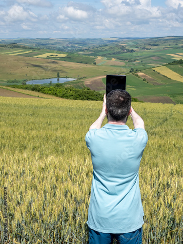 Man Using Tablet to Photograph Wheat Field and Scenic Countryside