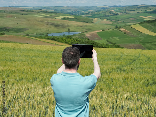 Man Using Tablet to Photograph Wheat Field and Scenic Countryside