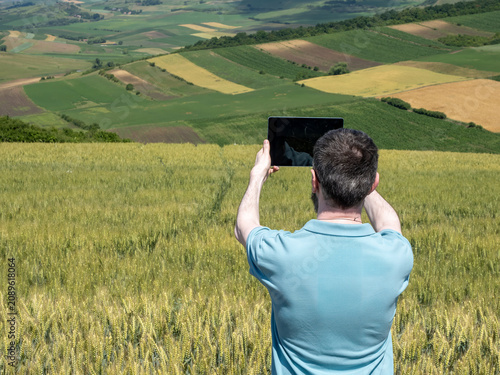 Man Using Tablet to Photograph Wheat Field and Scenic Countryside
