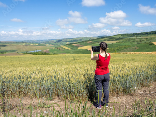 Woman Using Tablet to Photograph Scenic Wheat Field and Rural Landscape