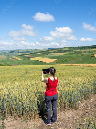 Woman Using Tablet to Photograph Scenic Wheat Field and Rural Landscape
