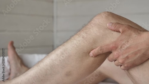 Close-up footage of man gripping painful knee while sitting in bed. Healthcare concept of injury and chronic joint pain