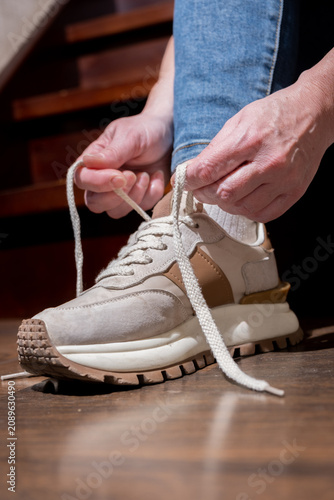Person ties shoelaces on a sneaker while sitting on stairs during the day in a home setting