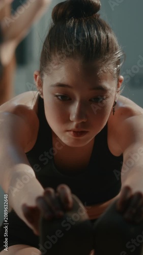 Girl in Athletic Outfit Performs Deep Forward Bend Stretch in Warm Up, Improving Hamstring Flexibility, Spinal Mobility. Training Routine, Required in Competitive Youth Gymnastics. Vertical Shot.