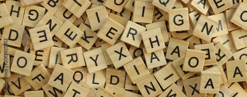 Pile of wooden tiles with various letters in big amount scattered on white board, closeup view
