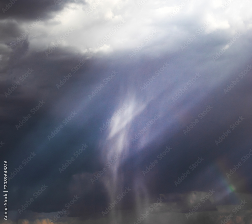 Naklejka premium Rain shafts illuminated by sunbeams with a small rainbow
