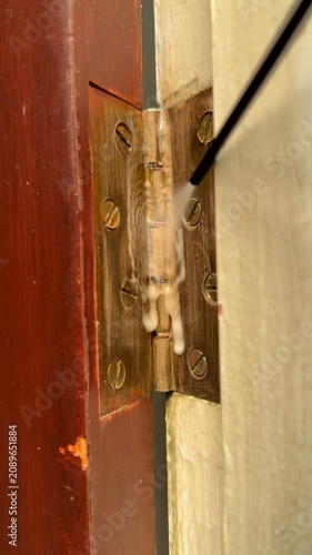 Vertical video social media - Closeup of release fluid being sprayed onto a sticking brass hinge, then the old wooden entry door moving back and forth to work the oil in.