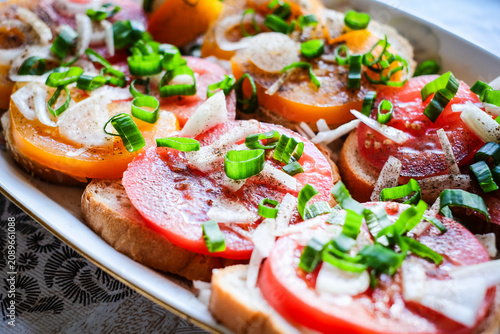 Close-up of fresh open-faced sandwiches topped with ripe sliced tomatoes, chopped white onion, green onions, black pepper, and a drizzle of oil on rustic bread. Traditional homemade summer snack 