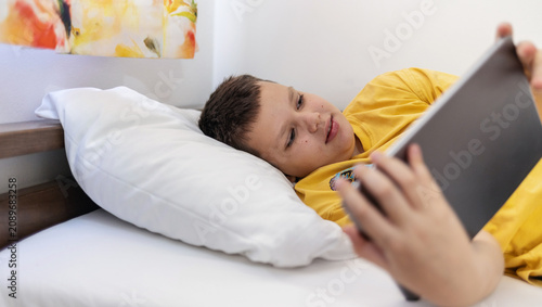 Young boy enjoys screen time in his bed, using a tablet computer to explore the digital world. Child using gadget, education and development.