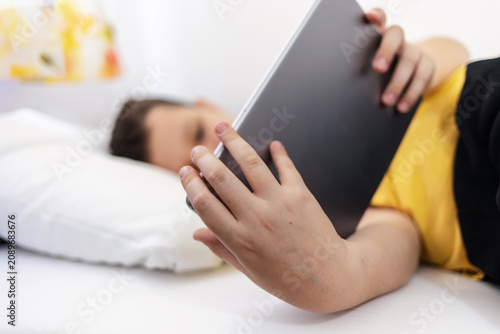 Boy lying in bed playing games on digital tablet at home. Happy little boy watching cartoons on digital tablet.