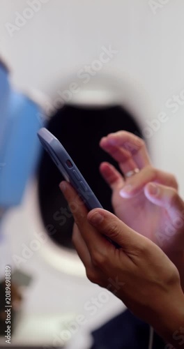 Close-up of woman passenger's hands using smartphone during night flight, browsing images or internet content for mobile entertainment, with blurred airplane window in background.