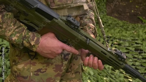 Soldier in camouflage standing guard at a concealed field position under camouflage netting. Military surveillance, security, and defensive operations in a field environment during armed conflict.