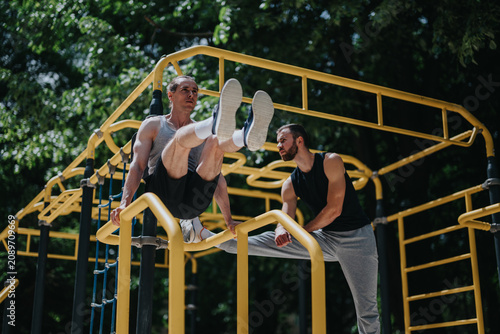 Foto Two athletic men perform a bodyweight L-sit and supported hold on yellow parallel bars during an outdoor workout