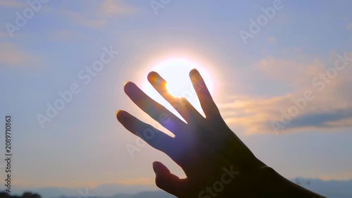 Silhouette of woman is waving her hand against the sunset, sunrise sky, sun is shining through fingers - sun lens flares, close up of moving female arm. Freedom, summer and inspiration concept