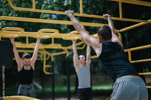 Photography Three adults exercising on yellow monkey bars, performing pull-ups and hanging movements