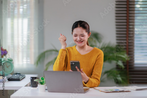 Fotografie Asian woman receiving good news on mobile phone, celebrating success and achieve