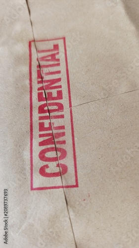 Macro view of a red confidential stamp on textured brown paper, symbolizing document security, privacy, classified information, corporate compliance, and legal protection.