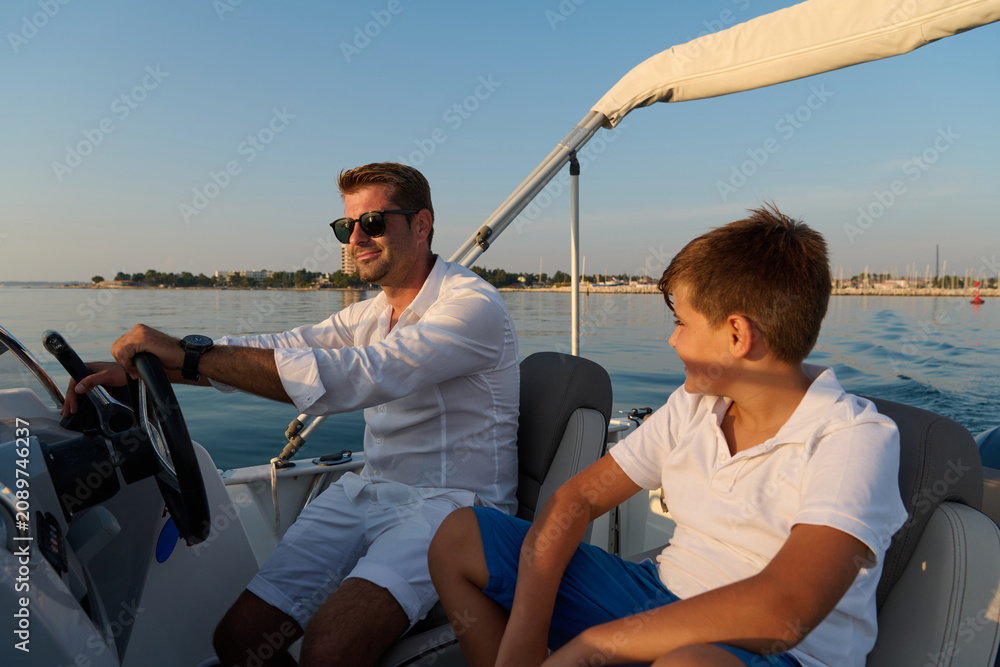 Obraz premium Father And Son Enjoying Summer Boat Ride On Calm Sea Near Coastal Marina During Golden Hour
