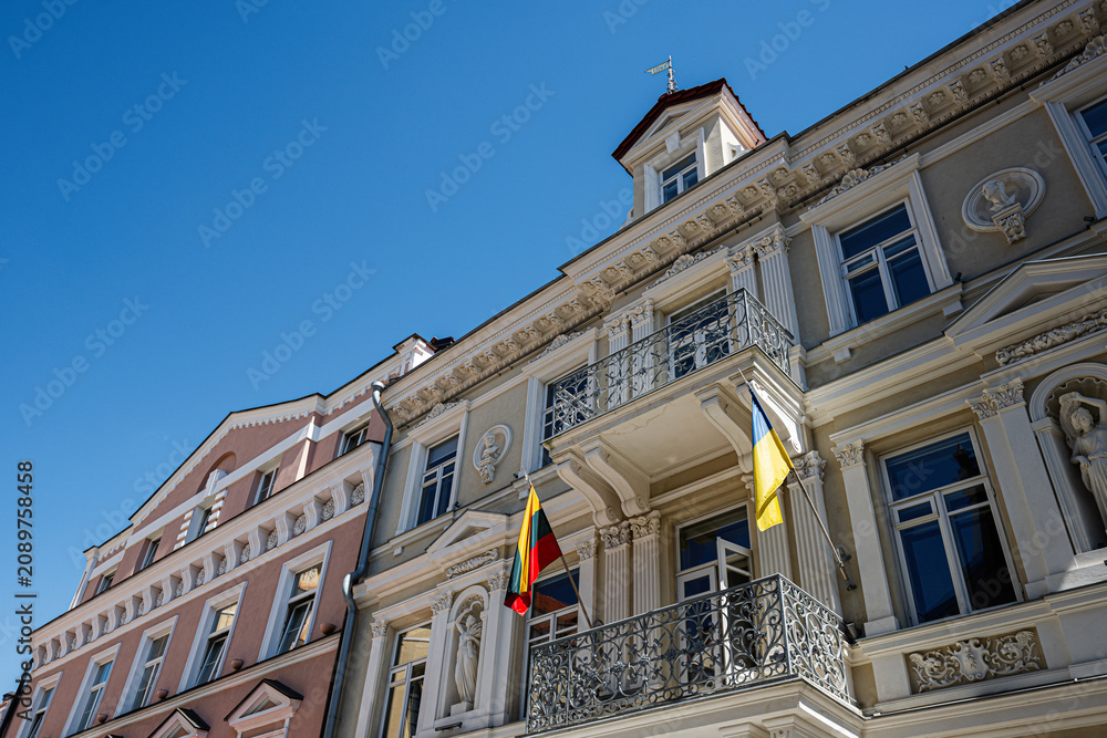 Obraz premium Historic neoclassical building facade with Lithuanian and Ukrainian flags on balcony in Vilnius, Lithuania under clear blue sky