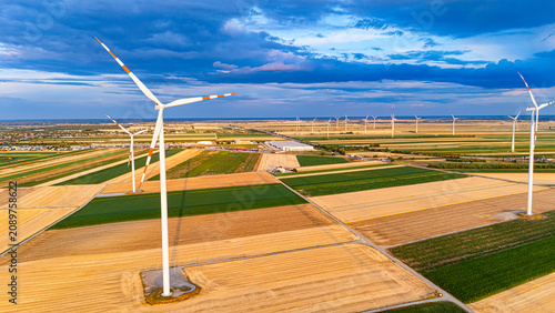 Wind turbines stand tall in the flat landscape during sunrise over fields. Wind turbines spin above vast fields during early morning. The sky has clouds and colors of dawn.