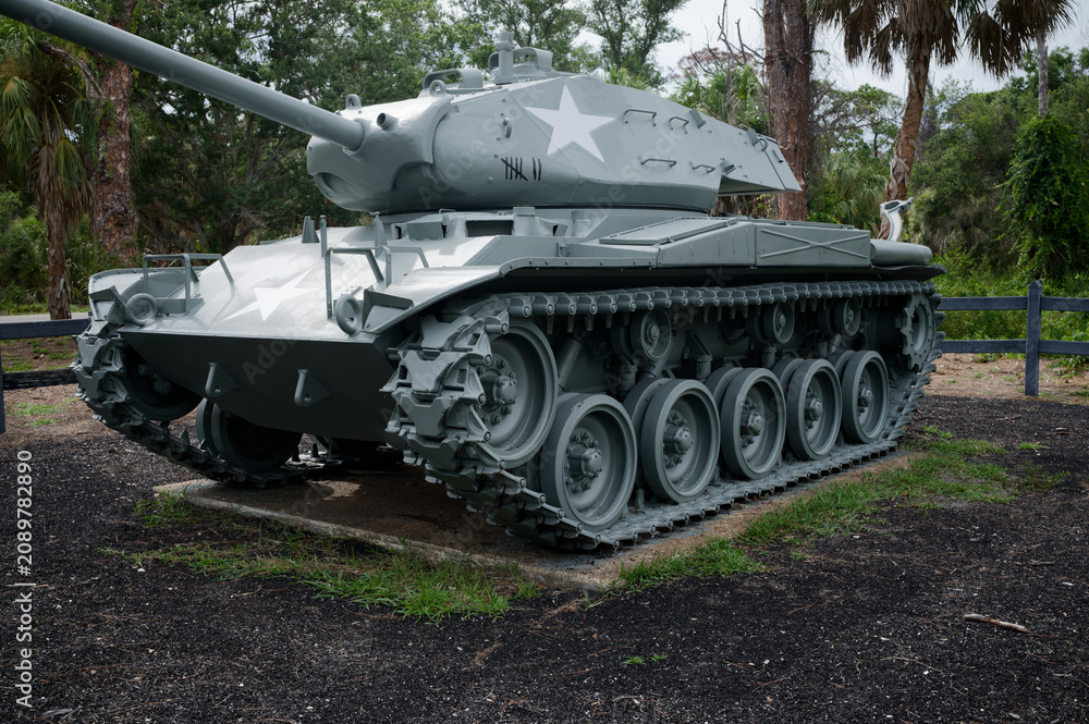 Fototapeta premium A restored historic military tank monument sits on display in a park setting with palm trees and wooden fencing. War Veterans Memorial Park In St. Petersburg, FL conveying military history, remembranc