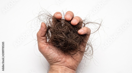 A human hand firmly holding a large messy clump of thin brown hair strands captured in a high resolution close up shot with natural lighting against a plain white surface.