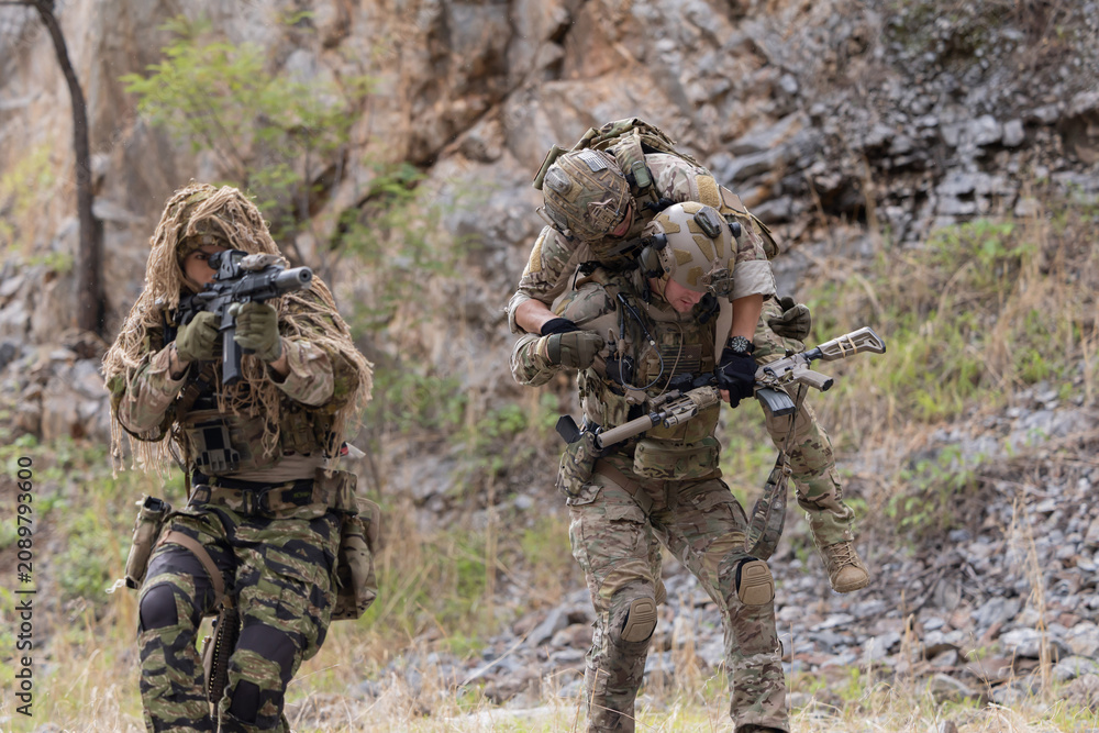Fototapeta premium Soldier carries injured comrade over rocky terrain