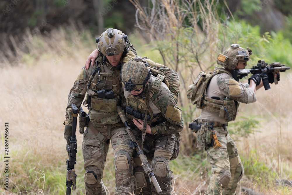 Fototapeta premium Soldier carries injured comrade over rocky terrain