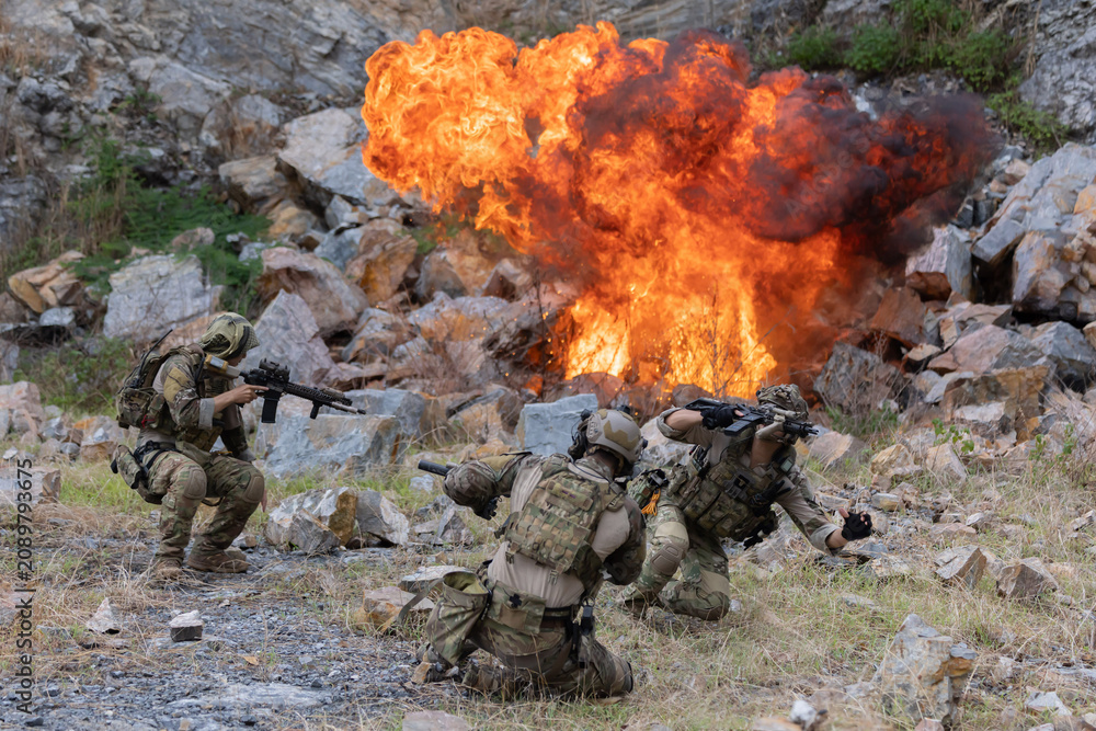 Fototapeta premium Military participate in a patrol in rocky terrain with explosion during combat scenario