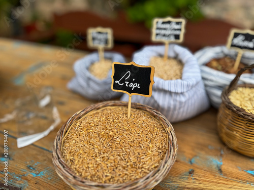 Traditional market display of grains and legumes in baskets and bags with greek handwritten blackboard signs. Selective focus on wheat grain bowl with a greek label that says 