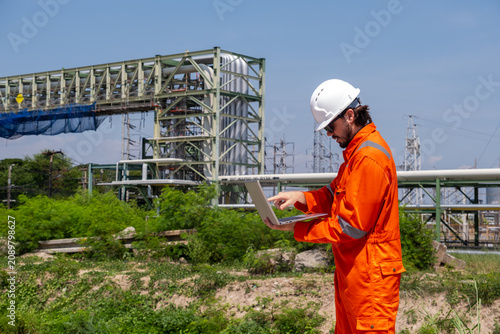 Foto Engineer works on laptop at industrial site during sunny day