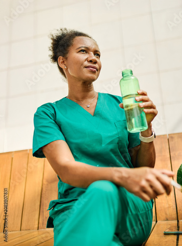 Young woman or a nurse or a doctor during office hours break enjoying a fresh salad and drinking water in a park during a sunny day while smiling and relaxing on a bench