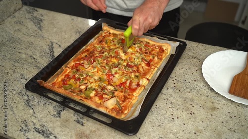 Homemade vegetable pizza being sliced with a pizza cutter on a baking tray.