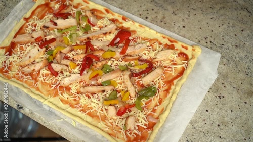 Homemade pizza preparation with tomato sauce, cheese, chicken, and colorful bell peppers before baking.