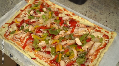 Homemade pizza preparation with tomato sauce, cheese, chicken, and colorful bell peppers before baking.