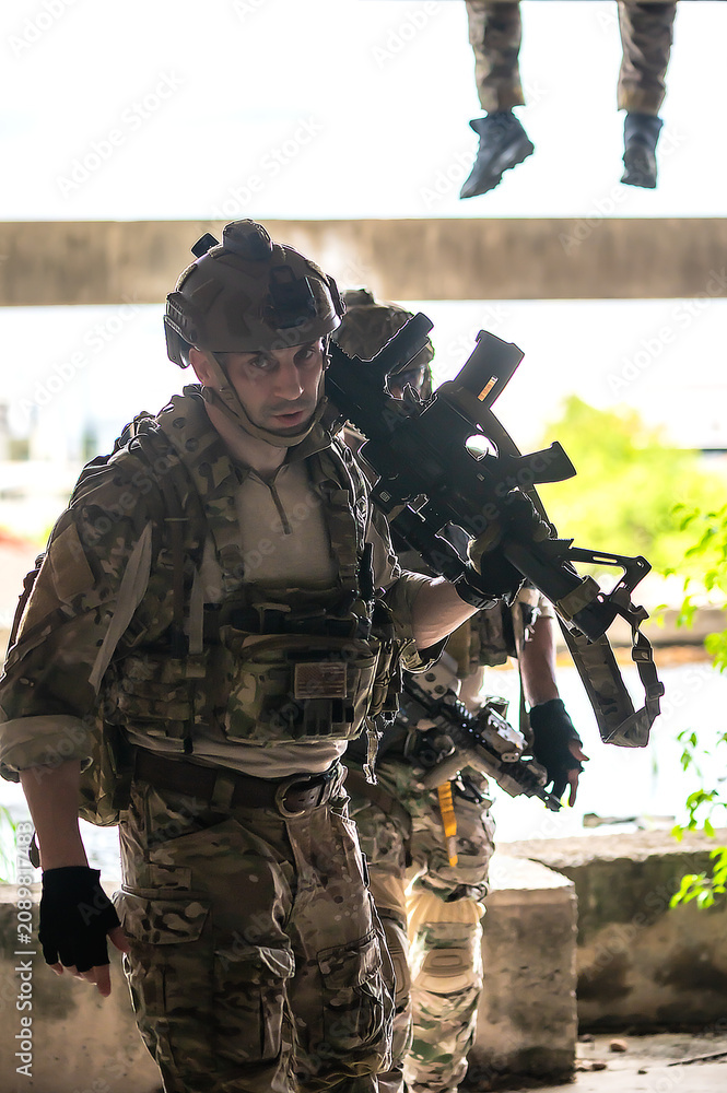 Fototapeta premium Male soldier in fully combat tactical military uniform and holding automatic war rifle, cautiously conducting a patrol and security sweep inside a ruined abandoned building