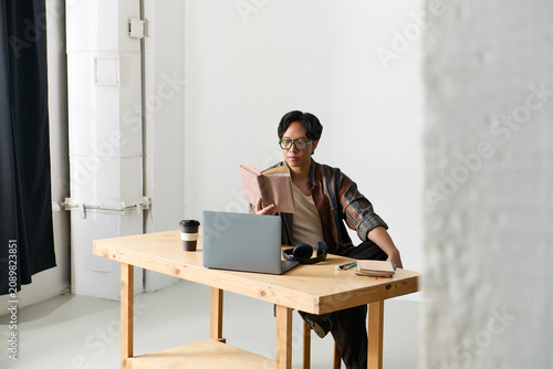 фотографія Charming young Asian man immersed in stylish reflection at a minimalist workspac