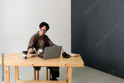 Photography Handsome young Asian man immersed in stylish work session at modern wooden desk