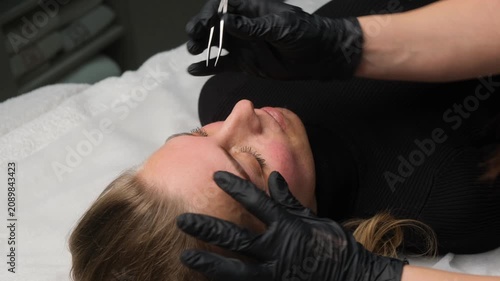 Esthetician plucking a client's eyebrows with tweezers during a professional beauty treatment