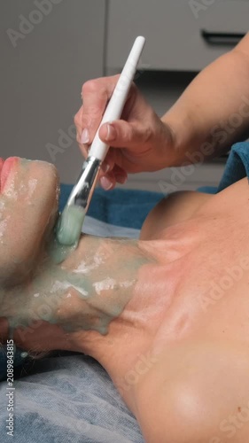 Aesthetician using a brush to apply a cosmetic alginate mask on a woman's neck in a beauty salon