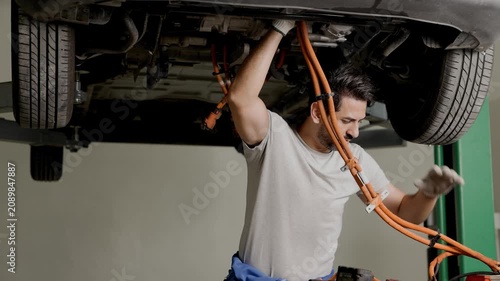 Professional worker service replacing EV car High volt power line cabling under the car in EV garage auto workshop
