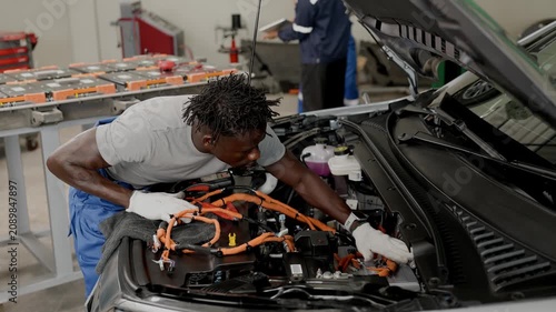 Professional African black male worker working service maintenance EV car in EV garage auto workshop, Cabling DC Inverter power line.