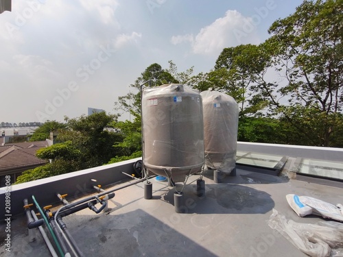 Фотография Two fiberglass material cylinder water storage tanks installed on a building concrete rooftop with PVC pipe installations